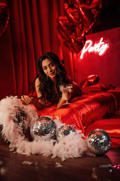 Attractive japanese lady in red underwear lying on silk sheet with champagne glass in a room decorated for Valentine\'s Day