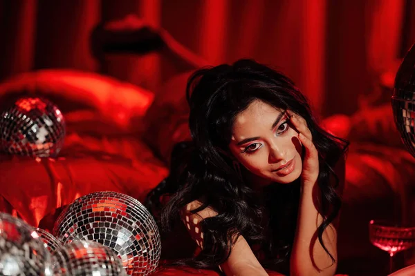 Sexy asian sensual model in red lace underwear posing with disco balls in a bed on Valentine\'s day