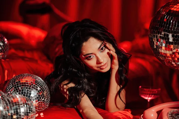 Curly black hair asian model with disco balls posing in bed on Valentine\'s day