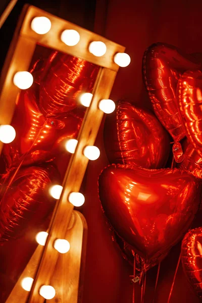 Extravagant bedroom luxury interior with love glamour decoration at Valentine day in studio. Balloons by heart shaped and at illuminated mirror romantic cozy atmosphere at vivid red background.