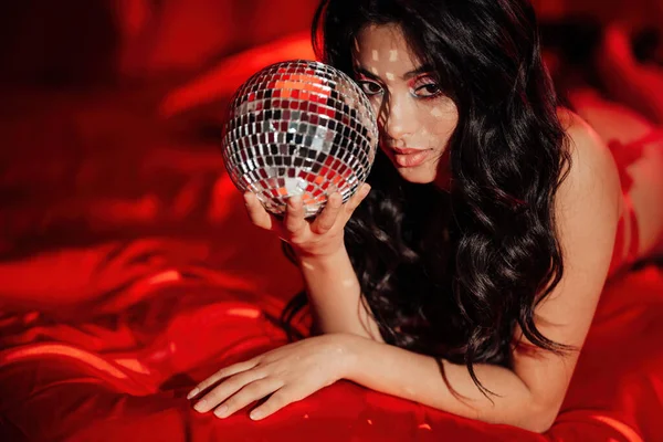 Curly black hair asian model with disco ball posing in bed on Valentine's day