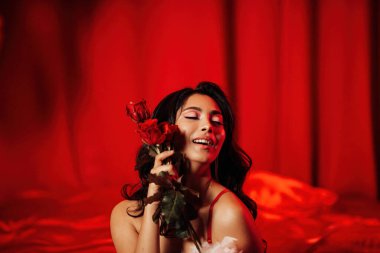 Sensual asian model posing with roses on red glamour background.