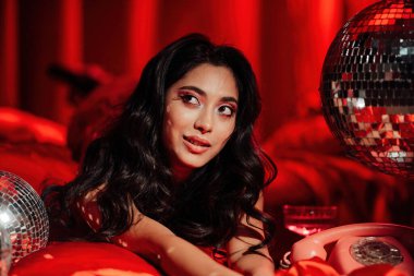 Sexy asian sensual model in red lace underwear posing with disco balls in bed on Valentine's day 