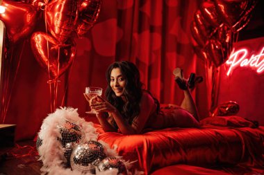 Attractive japanese lady in red underwear lying on silk sheet with champagne glass in a room decorated for Valentine's Day