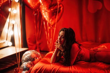 Sexy japanese lady in red underwear lying on silk sheet and looking the mirror in red bedroom 