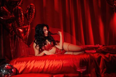 Attractive asian lady in red underwear lying on silk sheet in a room decorated for Valentine's Day