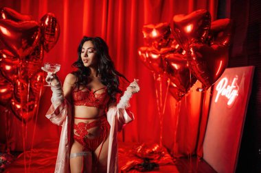 Brunette woman in sexy underwear posing with coupe glass of champagne in a room decorated for Valentine's Day