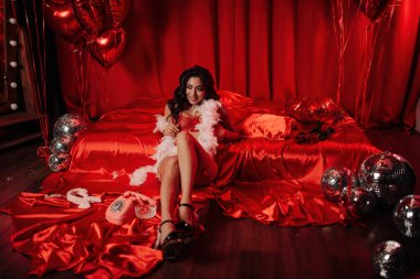 Sexy asian sensual model in red lace underwear and feather boa posing near the bed on Valentine's day  