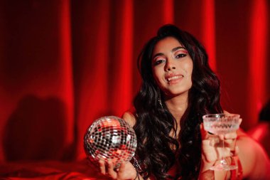 Curly black hair asian model with disco ball and champagne glass posing in bed on Valentine's day