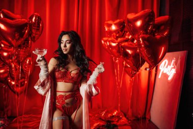 Brunette woman in sexy underwear posing with coupe glass of champagne in a room decorated for Valentine's Day