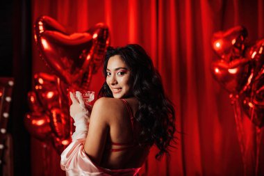 Brunette woman in sexy underwear posing with coupe glass of champagne in a room decorated for Valentine's Day