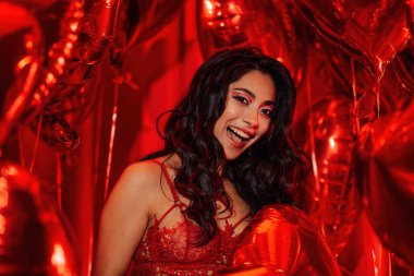 Happy brunette japanese woman with perfect skin in sexy lingerie posing with heart balloons in a red room  