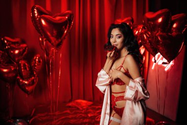 Beautiful asian black hair woman in sexy lingerie posing with cupcake in a room decorated for Valentine's Day