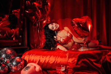 Sexy japanese lady in red underwear lying on silk sheet with balloon heart, posing on Valentine's day