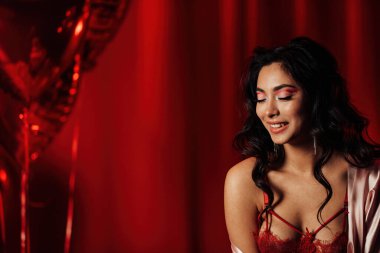 Close up portrait of attractive asian woman in lace underwear with eyes closed posing in a red room, copy space 