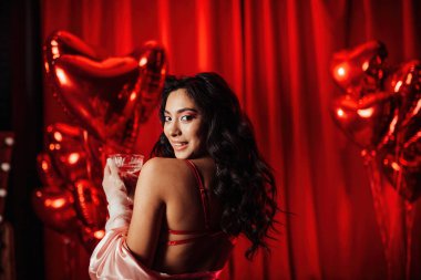 Sensual model brunette woman in sexy underwear posing with coupe glass of champagne in a room decorated for Valentine's Day