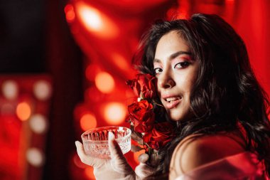 Brunette woman in sexy underwear posing with roses and coupe glass of champagne in a room decorated for Valentine's Day