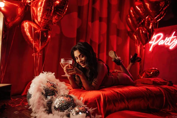 Attractive japanese lady in red underwear lying on silk sheet with champagne glass in a room decorated for Valentine\'s Day