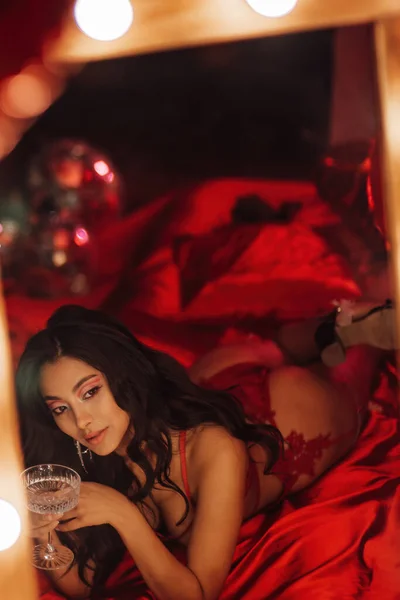 Japanese lady in red underwear lying on silk sheet with champagne glass in a room decorated for Valentine\'s Day