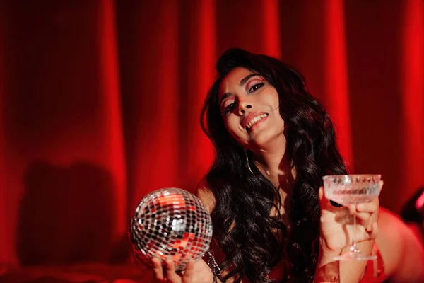 Curly black hair asian model with disco ball and champagne glass posing in bed on Valentine\'s day