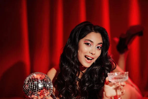 Curly black hair asian model with disco ball and champagne glass posing in bed on Valentine's day
