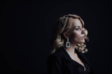 Young adult beauty woman in formal evening suit of black color with lace bra at thoughtful. Stylish blonde curly hair sensual model fashionista posing at studio in fashion pantsuit