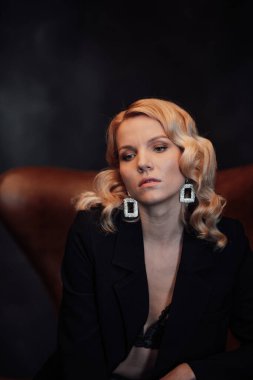 Young adult beauty woman in formal evening suit of black color with lace bra at thoughtful. Stylish blonde curly hair sensual model fashionista posing at studio in fashion pantsuit