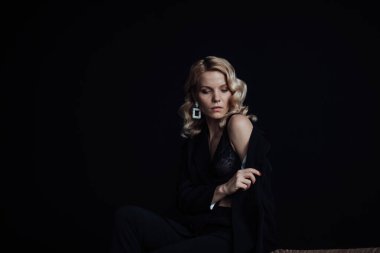 Young adult beauty woman in formal evening suit of black color with lace bra at thoughtful. Stylish blonde curly hair sensual model fashionista posing at studio in fashion pantsuit