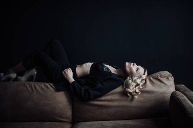 Young adult beauty woman in formal evening suit of black color with lace bra at thoughtful. Stylish blonde curly hair sensual model fashionista posing at studio in fashion pantsuit