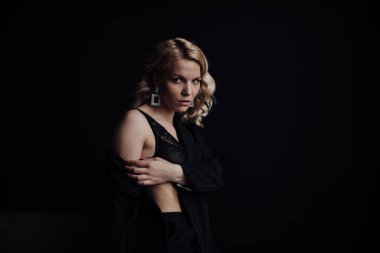 Young adult beauty woman in formal evening suit of black color with lace bra at thoughtful. Stylish blonde curly hair sensual model fashionista posing at studio in fashion pantsuit