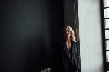 Adult beauty woman in formal evening suit of black color with lace bra taking photo for social media. Stylish blonde curly hair model fashionista posing in fashion pantsuit no shirt video calling