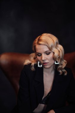 Young adult beauty woman in formal evening suit of black color with lace bra at thoughtful. Stylish blonde curly hair sensual model fashionista posing at studio in fashion pantsuit