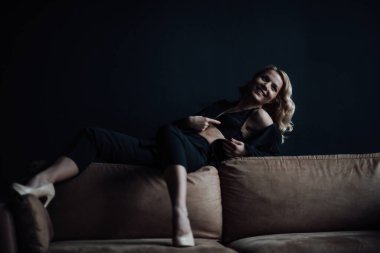 Young adult beauty woman in formal evening suit of black color with lace bra at thoughtful. Stylish blonde curly hair sensual model fashionista posing at studio in fashion pantsuit
