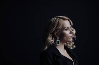 Young adult beauty woman in formal evening suit of black color with lace bra at thoughtful. Stylish blonde curly hair sensual model fashionista posing at studio in fashion pantsuit