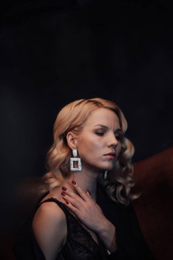 Young adult beauty woman in formal evening suit of black color with lace bra at thoughtful. Stylish blonde curly hair sensual model fashionista posing at studio in fashion pantsuit