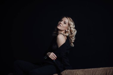Young adult beauty woman in formal evening suit of black color with lace bra at thoughtful. Stylish blonde curly hair sensual model fashionista posing at studio in fashion pantsuit
