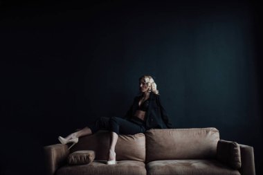 Young adult beauty woman in formal evening suit of black color with lace bra at thoughtful. Stylish blonde curly hair sensual model fashionista posing at studio in fashion pantsuit