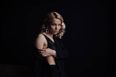 Young adult beauty woman in formal evening suit of black color with lace bra at thoughtful. Stylish blonde curly hair sensual model fashionista posing at studio in fashion pantsuit