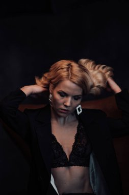 Young adult beauty woman in formal evening suit of black color with lace bra at thoughtful. Stylish blonde curly hair sensual model fashionista posing at studio in fashion pantsuit