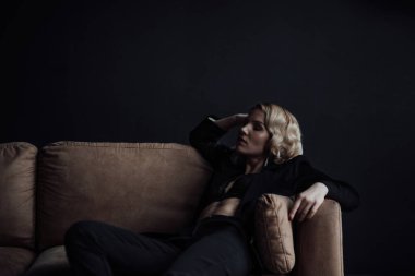 Young adult beauty woman in formal evening suit of black color with lace bra at thoughtful. Stylish blonde curly hair sensual model fashionista posing at studio in fashion pantsuit