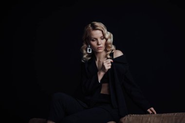 Young adult beauty woman in formal evening suit of black color with lace bra at thoughtful. Stylish blonde curly hair sensual model fashionista posing at studio in fashion pantsuit