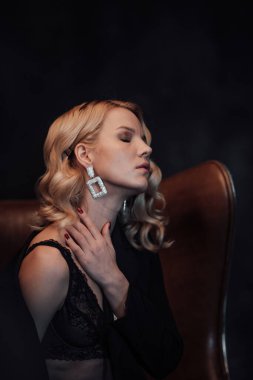 Young adult beauty woman in formal evening suit of black color with lace bra at thoughtful. Stylish blonde curly hair sensual model fashionista posing at studio in fashion pantsuit