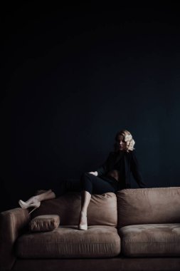 Young adult beauty woman in formal evening suit of black color with lace bra at thoughtful. Stylish blonde curly hair sensual model fashionista posing at studio in fashion pantsuit