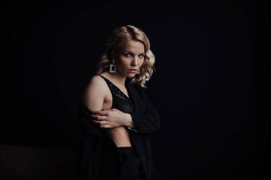 Young adult beauty woman in formal evening suit of black color with lace bra at thoughtful. Stylish blonde curly hair sensual model fashionista posing at studio in fashion pantsuit