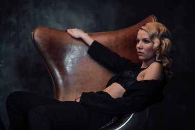 Young adult beauty woman in formal evening suit of black color with lace bra at thoughtful. Stylish blonde curly hair sensual model fashionista posing at studio in fashion pantsuit
