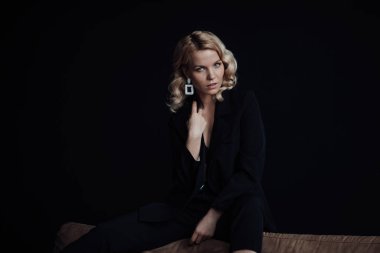 Young adult beauty woman in formal evening suit of black color with lace bra at thoughtful. Stylish blonde curly hair sensual model fashionista posing at studio in fashion pantsuit