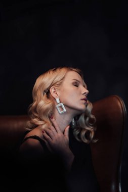 Young adult beauty woman in formal evening suit of black color with lace bra at thoughtful. Stylish blonde curly hair sensual model fashionista posing at studio in fashion pantsuit