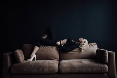 Young adult beauty woman in formal evening suit of black color with lace bra at thoughtful. Stylish blonde curly hair sensual model fashionista posing at studio in fashion pantsuit