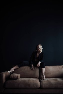 Young adult beauty woman in formal evening suit of black color with lace bra at thoughtful. Stylish blonde curly hair sensual model fashionista posing at studio in fashion pantsuit