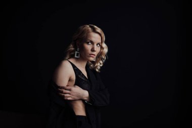 Young adult beauty woman in formal evening suit of black color with lace bra at thoughtful. Stylish blonde curly hair sensual model fashionista posing at studio in fashion pantsuit